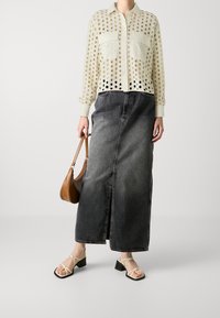 Lightweight sheer blouse with circular cutouts, paired with a high-waisted dark denim skirt. Finished with strappy heels and a brown bag.