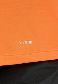 Orange ClimaCool fabric, breathable mesh texture, features white logo at hem, with black contrasting fabric below.