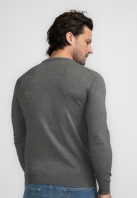 Grijze gebreide trui met een ronde hals en lange mouwen. De textuur is lichtjes gebobbeld en het heeft een geribbelde onderrand. Geen zichtbare patronen.