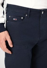Navy blauwe katoenen broek met een gladde textuur, voorzien van een voorvak, zilveren knopen en een klein merkembleem op het vak.