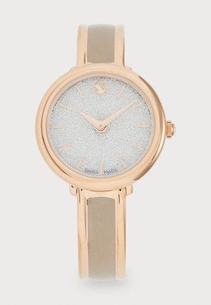 Roségoldfarbene Uhr mit rundem Gehäuse, glitzerndem silbernen Ziffernblatt und schlanken Zeigern. Besitzt ein glattes, beiges Silikonarmband. Schweizer Qualität.