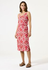 Rode en roze gemusterde midi-jurk met spaghettibandjes, strakke taille, zijsplit en bloemenprint. Gecombineerd met bruine sandalen.