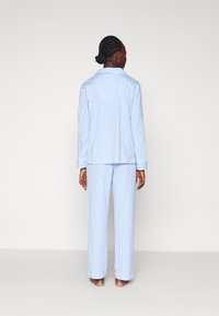 Pajamaset v modro-belem prugastem vzorcu, izdelan iz mehke tkanine; vsebuje srajco z ovratnikom z dolgimi rokavi in hlače ravnega kroja, vidnimi šivi.