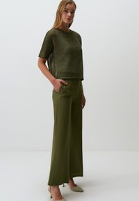 Haut tricoté à manches courtes de couleur vert olive associé à un pantalon ample de couleur vert olive. Tissu texturé et design taille haute, avec des poches latérales.