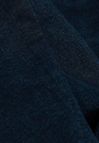 Tissu en denim bleu foncé avec une texture visible et des plis diagonaux, montrant le tissage du matériau et les variations de couleur.