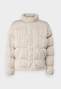Polstret jakke i lyse beige stof med høj krave, prydet med en quiltet design og et lille logo-patch i kanten.