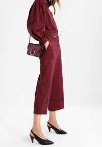 Burgundské zkrácené kalhoty, spárované s odpovídajícím topem s nafouknutými rukávy a černými lodičkami s otevřenou patou a špičkou. Kabelka s detailním řetízkovým popruhem.