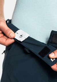 Regulowany materiałowy pasek w ciemnoniebieskim kolorze z białym zapięciem na rzep i metalowym zatrzaskiem. Gładka tekstura, część odzieży outdoorowej.