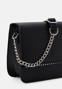 Černá kabelka z umělé kůže s pevnou strukturou, řetízkovým popruhem a s kovovými cvoky na přední straně. Hladká textura a minimalistický design.