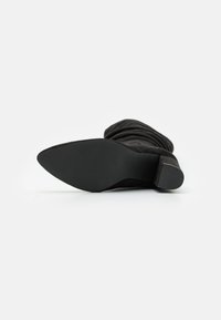 Svart nubuck ankelstøvlett med en slouchy design, spiss tå og lav stablet hæl. Sålen er teksturert for grep.