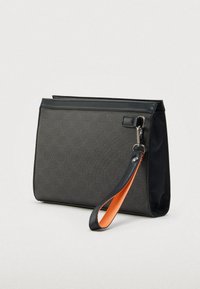 Musta suorakaiteenmuotoinen rannetasku hienovaraisella kuviolla, musta nahkareunus ja irrotettava musta hihna, jossa oranssi sisävuori.