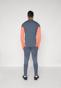 Sportski outfit koji se sastoji od tamnosive majice dugih rukava sa koraljnim rukavima i uskih tajica koje se savršeno uklapaju, izrađena od glatkog, rastezljivog materijala.
