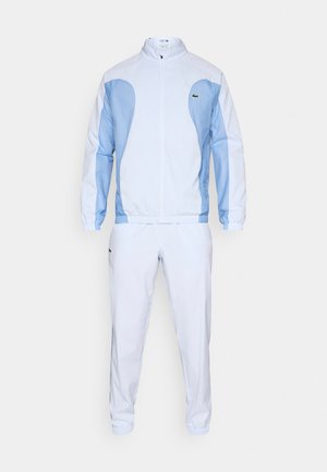 Trainingspak met een lichtblauw-wit ontwerp, gemaakt van gladde stof, met elastische manchetten en een klein logo op de borst.