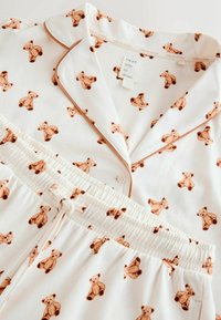 Cotton pajama set featuring a white background with small brown teddy bear prints. Includes a button-up top and elastic waist bottoms with drawstring.