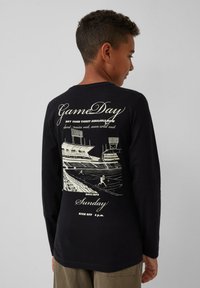 Czarny t-shirt z długim rękawem z graficznym nadrukiem przedstawiającym scenę z stadionu oraz tekstem opisującym wydarzenie w dniu meczu na plecach.