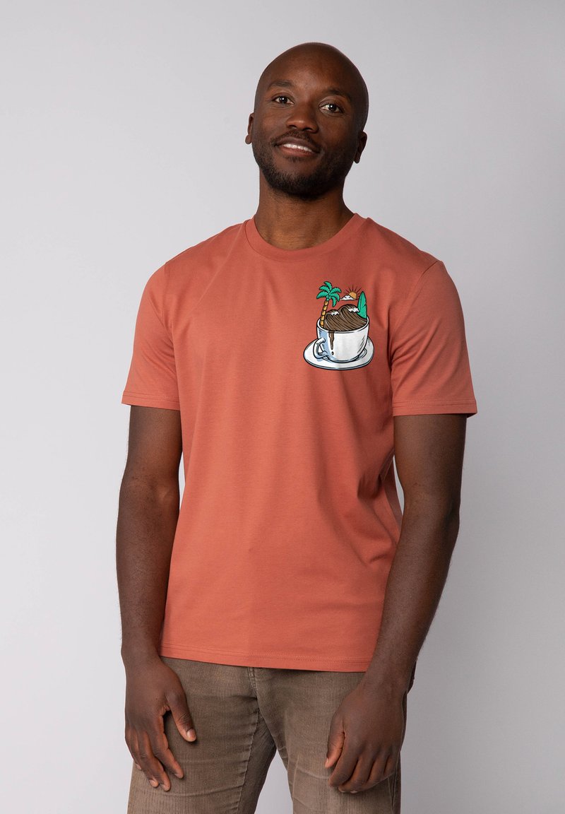 T-shirt en coton couleur rouille avec un design brodé représentant une tasse avec un dessert et des palmiers sur le côté gauche de la poitrine.