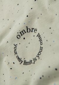 Camiseta de tela verde claro con patrones moteados en azul y negro. Presenta un texto circular: "Tu único límite es tu mente."