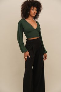 Zelený dlouhý rukáv cropped top s hlubokým výstřihem do V, spárovaný s černými kalhotami s vysokým pasem a širokými nohavicemi. Hladká textura, minimální detaily.