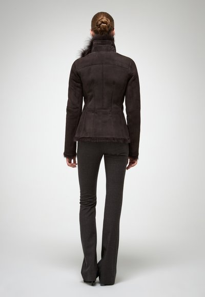Chaqueta de ante marrón con cuello alto, borde de piel, ajuste entallado y dobladillo acampanado, combinada con pantalones acampanados de un gris oscuro.