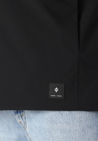 Svart jakke med en matt tekstur, med et kvadratisk merke på kanten og paret med lys blå denim.