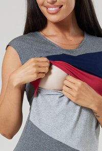Gray, red, and navy color-blocked shirt with short sleeves. Fabric appears soft. A person lifts the shirt to reveal a beige undergarment.