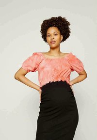 Blusa cor-de-rosa com mangas balão e decote redondo, combinada com uma saia preta justa, com tecido liso e detalhes franzidos na cintura.