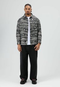 Zwart-wit patroon jas met een spreidkraag over een wit T-shirt, gecombineerd met losse zwarte broek en zwarte schoenen met roze veters.