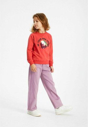 Sweatshirt rouge avec texte imprimé et un graphisme multicolore, associé à un pantalon violet clair et des baskets blanches. Coupe décontractée et design moderne.