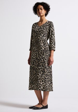 Abito con stampa leopardata, maniche a tre quarti, scollo a V, silhouette fluida, nei toni beige e neri, abbinato a ballerine nere.