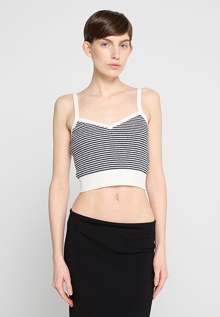 Gestreifter Crop-Top in Weiß und Marineblau mit dünnen Trägern, ausgestattet mit einem gerippten Bund und einem V-Ausschnitt, kombiniert mit einem schwarzen, figurbetonten Rock.