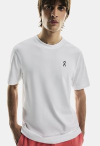 Vit bomull t-shirt med rund hals, korta ärmar och en liten svart logotyp på bröstet. Slät textur, avslappnad passform.