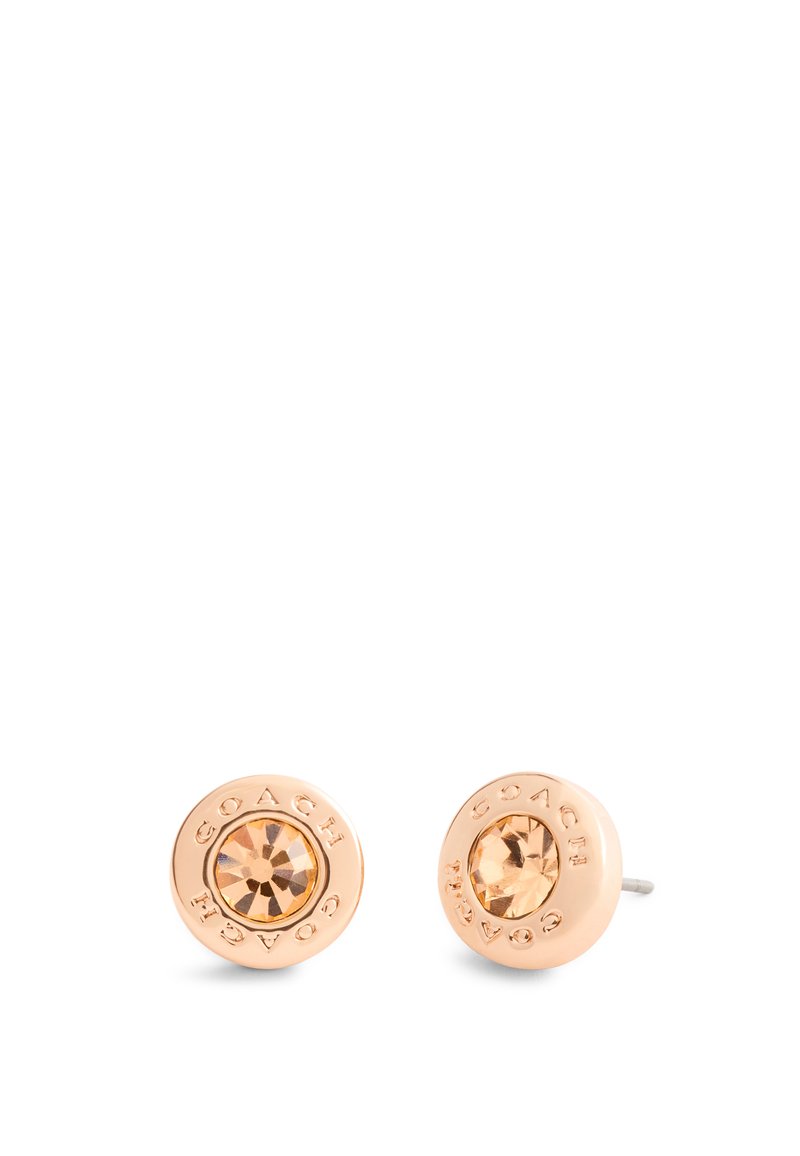Boucles d'oreilles en or rose avec une pierre centrale facettée de couleur ambre. Le nom de la marque « COACH » gravé entoure la pierre. Finition lisse.