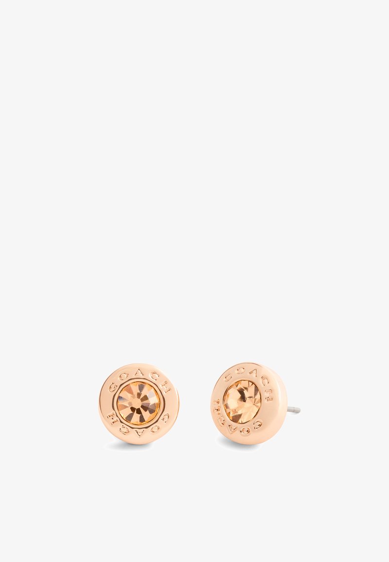 Boucles d'oreilles en or rose avec une pierre centrale facettée de couleur ambre. Le nom de la marque « COACH » gravé entoure la pierre. Finition lisse.