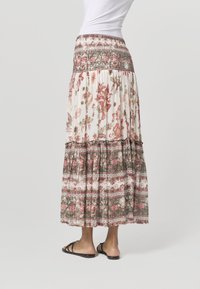 Kukkainen maksihame, jossa on smokkikoristeltu vyötärö ja valkoisia, vaaleanpunaisia ja vihreitä kuvioita. Hameessa on kerrokselliset röyhelöt ja koristeellinen reunus helmassa.