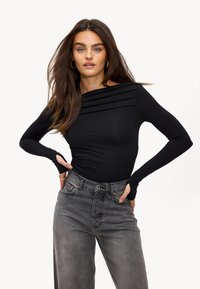 Zwarte lange mouwen top met geplooid detail rond de halslijn, gecombineerd met hoog-talje grijze jeans met een klassieke vijf-pocket ontwerp.