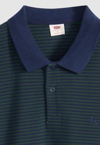 Πόλο πουκάμισο με ρίγες σε μπλε και πράσινο χρώμα, υφασμένο με υφή. Διαθέτει γιακά, κλείσιμο με τρία κουμπιά και κεντημένο λογότυπο στο στήθος.