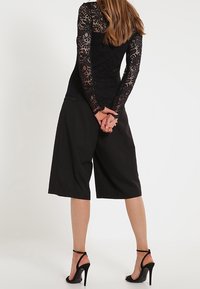 Top in pizzo nero con maniche lunghe e design sul retro, abbinato a culotte nere a gamba larga e sandali neri con tacco.