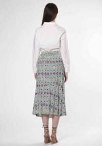 Chemise blanche à col avec une jupe maxi à motifs colorés présentant des formes géométriques en turquoise, rose et jaune, avec une taille froncée.