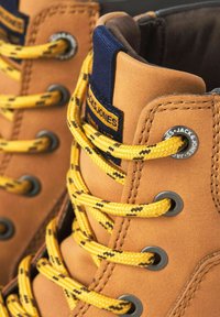 Detailní záběr na hnědé turistické boty se žlutými a černými tkaničkami provlečenými kovovými očky, s textilní štítkem.