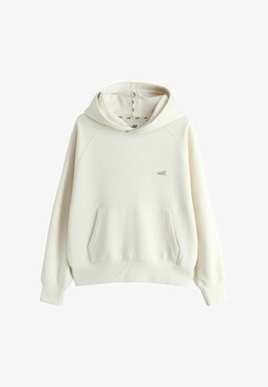 Cream-colored hoodie with front pouch pocket and small "self." logo on the left chest, displayed on a white background.