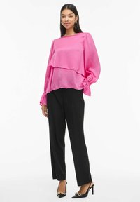 Rosa lagdelt bluse med lange ermer, innsnoede mansjetter; kombinert med høytlivede svarte bukser og svarte spisse hæler med gullaccenter.