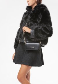Chaqueta negra de piel sintética con detalles de cuero, combinada con una falda negra texturizada. Un pequeño bolso bandolera negro de cuero con herrajes dorados.