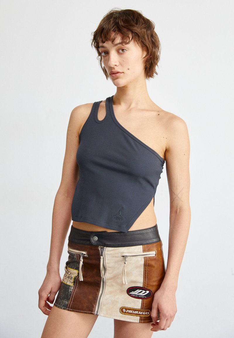 Harmaa ribbattu croptop, jossa on yksi olkahihna ja kaarrepinta, yhdistettynä moniväriseen nahkahameeseen, jossa on vetskareita ja päällekkäin ommeltuja yksityiskohtia.
