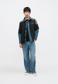 Farmershajtó fekete és kifakult kék mintával, laza, világoskék farmerrel párosítva. Az összeállítást szürke tornacipő egészíti ki.