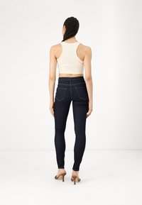 Jeans oscuros de cintura alta con un diseño ajustado, que cuentan con dos bolsillos traseros y costuras en contraste, combinados con un top corto beige.