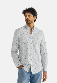 Lichtblauw button-up shirt met een verspreid geometrisch patroon in donkerdere tinten, gemaakt van een gladde stof, met een klassieke kraag en manchetten.