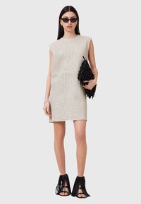 Beige perforeret mini kjole med cap ærmer, parret med en sort frynset clutch og matchende frynset hæl sandaler. Glat overflade generelt.