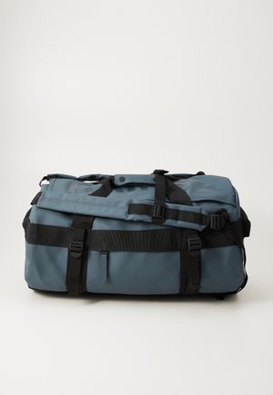 Dufflebag i teksturert blått materiale med svarte stropper. Har flere spenner, et håndtak på toppen og et logo-patch på siden.