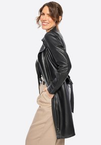 Chaqueta de cuero negra de manga larga con cremallera asimétrica, cuello con muesca y bolsillos frontales, combinada con pantalones de talle alto beige.