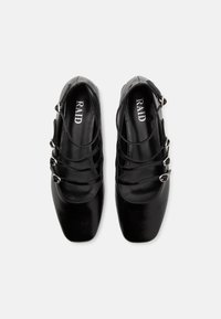 Ballerines Mary Jane en cuir verni noir, à bouts carrés, avec trois fines lanières munies de boucles argentées, et logo de la marque RAID à l'intérieur.